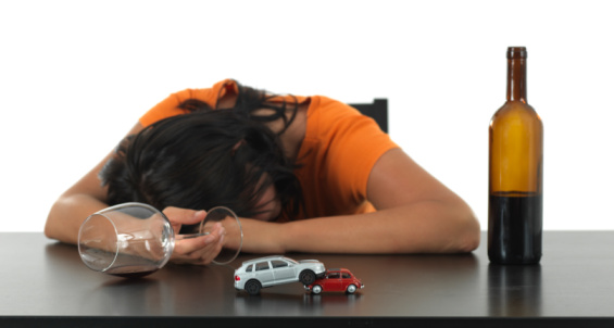 Woman with a bottle of wine asleep at a table with two toy cars